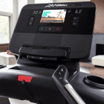 Console of the Life Fitness Club Series Plus Treadmill. This features a digital screen with a woman leading a workout, a tablet holder, a speaker and several buttons